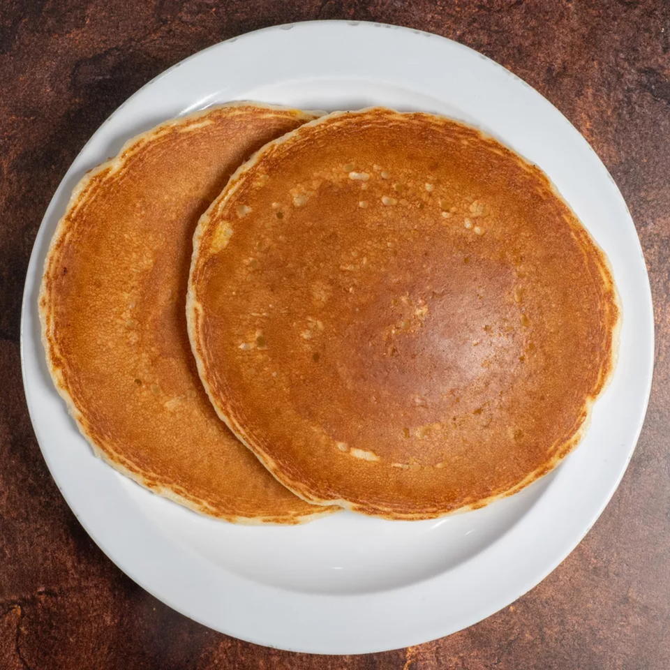 Two golden-brown pancakes on a white plate, viewed from directly above.