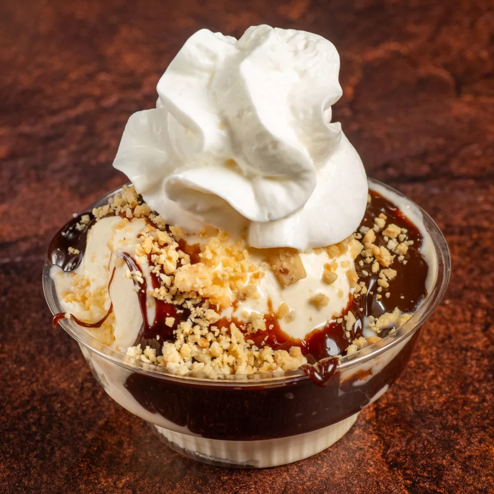 Vanilla ice cream sundae with chocolate syrup, crushed nuts, and whipped cream in a clear cup.