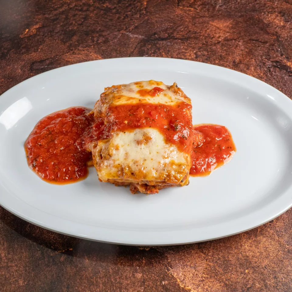 A rectangular piece of lasagna with melted cheese and red sauce on a white oval plate.